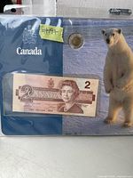 Photo showing a sealed package containing a $2 Canadian banknote and a $2 Canadian coin with a polar bear design, along with a Canada label.