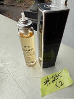 Photo showing two Chanel No. 5 perfume bottles; one is a refill bottle with clear glass and yellow liquid, the other is a black and silver spray bottle with Chanel logo on the cap.