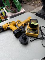 Photo showing two yellow DeWalt cordless drills, one charger with battery attached, and one separate battery pack on a gray table.