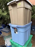 Photo showing one tan and one light blue Rubbermaid Roughneck totes stacked, both with lids and normal wear.