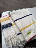 Two folded white sofa blankets with colored horizontal stripes and fringed edges on a table.