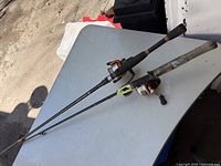Two vintage fishing poles laid out on a table, showing the length, grips, reels, and general condition.