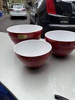 Three ceramic mixing bowls displayed together on a flat surface outdoors, showing the size variation and colors.