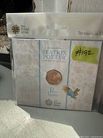 Photo of a 50p coin featuring Peter Rabbit from Beatrix Potter, in original Royal Mint packaging with decorative character pattern and branding.