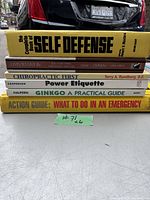 Photo showing six books stacked horizontally with titles visible: 'The Complete Book of Self Defense', 'Lists to Live By', 'Chiropractic First', 'Power Etiquette', 'Ginkgo: A Practical Guide', and 'Action Guide: What to Do in an Emergency'.