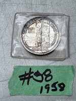 Photo of 1958 Canadian silver dollar coin in protective sleeve with tag '#08 1958' visible.