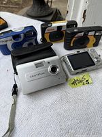 Five vintage cameras including Kodak disposable cameras, Polaroid instant camera, Centrios and Sony digital camera on white surface.