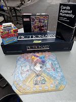 Overview of all games including Pictionary boxes, Cards Against Humanity box, various small card game boxes (Uno, Alphabet, Marvel) and Cribbage board