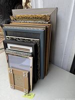 Stacked picture frames of various sizes and designs, showing ornate gold, black, silver, and gray frames.