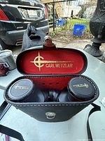 Open black leather binocular case with red interior lining showing the Carl Wetzlar logo and binoculars inside with lens caps on.