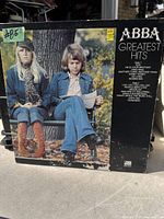 Photo of ABBA Greatest Hits LP cover showing the album artwork and tracklist on the front, with visible signs of wear.