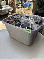 Plastic bin filled with assorted LEGO parts including bricks, plates, wheels, and sealed accessory bags.