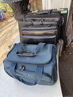 Photo of five bags stacked including blue tote, leather briefcases, and laptop cases.