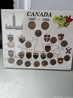 Coins arranged on a white display card labeled Canada 1867-1992 with provincial shields and a map, each coin placed below corresponding province abbreviation.