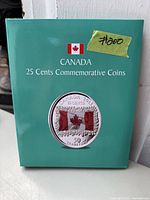 Green album folder with front cover featuring a 2015 Canadian 25 cents commemorative coin with colored Canadian flag design and price tag.