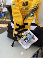 Close-up of yellow and black Fluid adult life jacket, showing size label Adult Large and brand logos. Tag and instruction booklet attached.