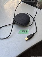 Black Google Nest Mini smart speaker on a metal surface with attached black USB cable, USB-A connector visible.