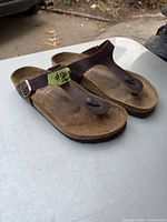 Front perspective of both sandals resting on a table showing leather straps and footbed