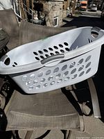 White Sterilite laundry basket angled view on a chair outdoors showing oval side holes and top handle.