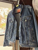 Blue denim Levi's ladies jean jacket hanging, showing front side with buttons and pockets visible.