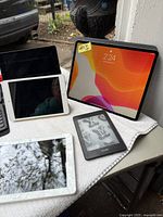 Five tablets and one Kindle e-reader arranged on a tablecloth; Bluetooth keyboard case at left