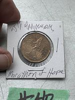 Photo of the 2005 Canadian $1 coin featuring Terry Fox commemorating the 25th anniversary of the Marathon of Hope, held in a staple-secured white cardboard holder inscribed with handwritten notes.