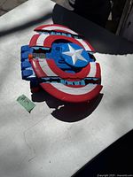 Top and front angled view of the red, white, blue Captain America shield shaped Nerf blaster showing star emblem and dart barrel
