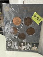 Front cover of the coin collection album showing six penny coins under clear plastic. The black cover has gold text and small portraits of British monarchs at the bottom.