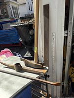 Side view of the axe with wooden handle, metal square tool, and pick axe head on a white surface outdoors.