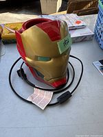 Front view of the Iron Man helmet-shaped Scentsy warmer showing the cord and wiring, with a green sticker indicating item number.
