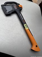 Photo showing entire Fiskars X11 splitting axe with orange and black handle lying on a gray surface, with blade cover intact.