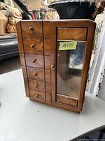 Front view of the vintage burled walnut jewellery case showing six small drawers and the etched glass door with keyhole and wooden frame.