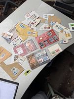 Layout of various vintage stamps on envelopes, loose on table, and in small plastic sleeves.