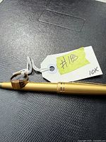 Ring resting on gold pen with visible tag '#182 10K'