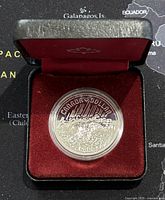 Front view of the silver dollar coin inside its display case with burgundy interior.