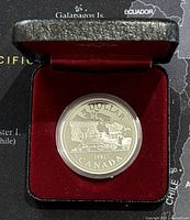 Silver Canadian dollar coin in protective capsule displayed inside a black case lined with red velvet.