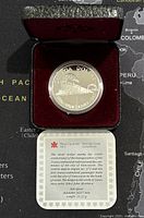 Silver Canadian dollar coin in red velvet presentation case with certificate visible below.