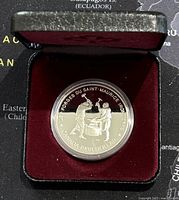 Front view of the coin inside a red velvet-lined black display case showing the reverse side with blacksmith imagery.