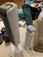 Two tower air purifiers in a room with varied household items in background, showing overall size and appearance.