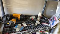 Overview of all pneumatic tools and accessories on shelf including yellow Bostitch nailer, two grey staple guns, oil bottle, box of staples, and sealed fittings