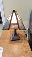 Front and side view of Art Deco style lamp showing stained glass shade with geometric pattern and bronze base on wooden table.