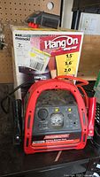 Front view of MotoMaster booster pack in front of Hang On shop vac box