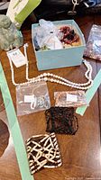 Photo showing assorted beads in plastic bags, strands of beads laid out on a wooden surface, and a blue box containing more beads.