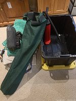 Wide view of all camping equipment including tarps, green chair bag, black storage bin with red air pump inside