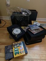 Photo showing loose DVDs and CDs on and around black carrying cases, including 'On the Buses' DVD collection and some discs loose on top of cases.