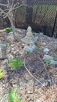 Full view of the cement pagoda placed outdoors in a garden bed surrounded by stones and plants.