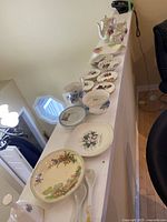 View of the entire tea ware collection arranged in a row on a table showing plates, teapot, cups, and accessories