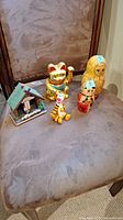 View of all collectibles including nesting dolls (with numbers 5 and 7), Japanese lucky cat, Tigger figurine, and Swiss style motion thermometer on chair seat