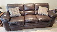 Full front view of the three-seat dark brown faux leather sofa with two striped pillows.
