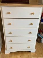 Front view of the white 5-drawer dresser showing wooden knobs and surface condition